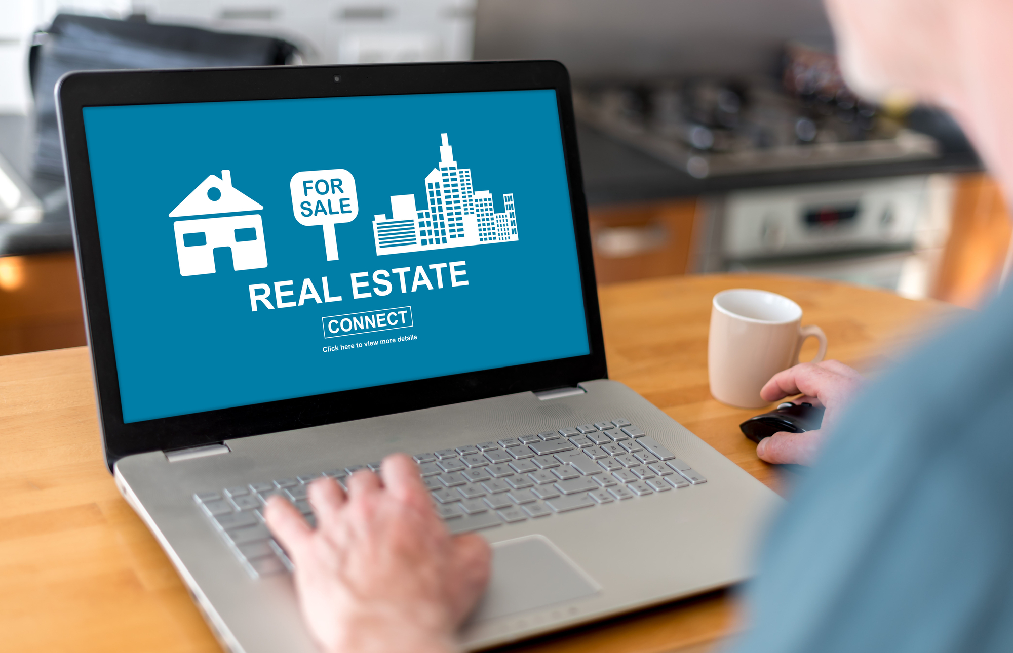 A person sits at their work desk, using a laptop which displays a screen that reads “real estate.”