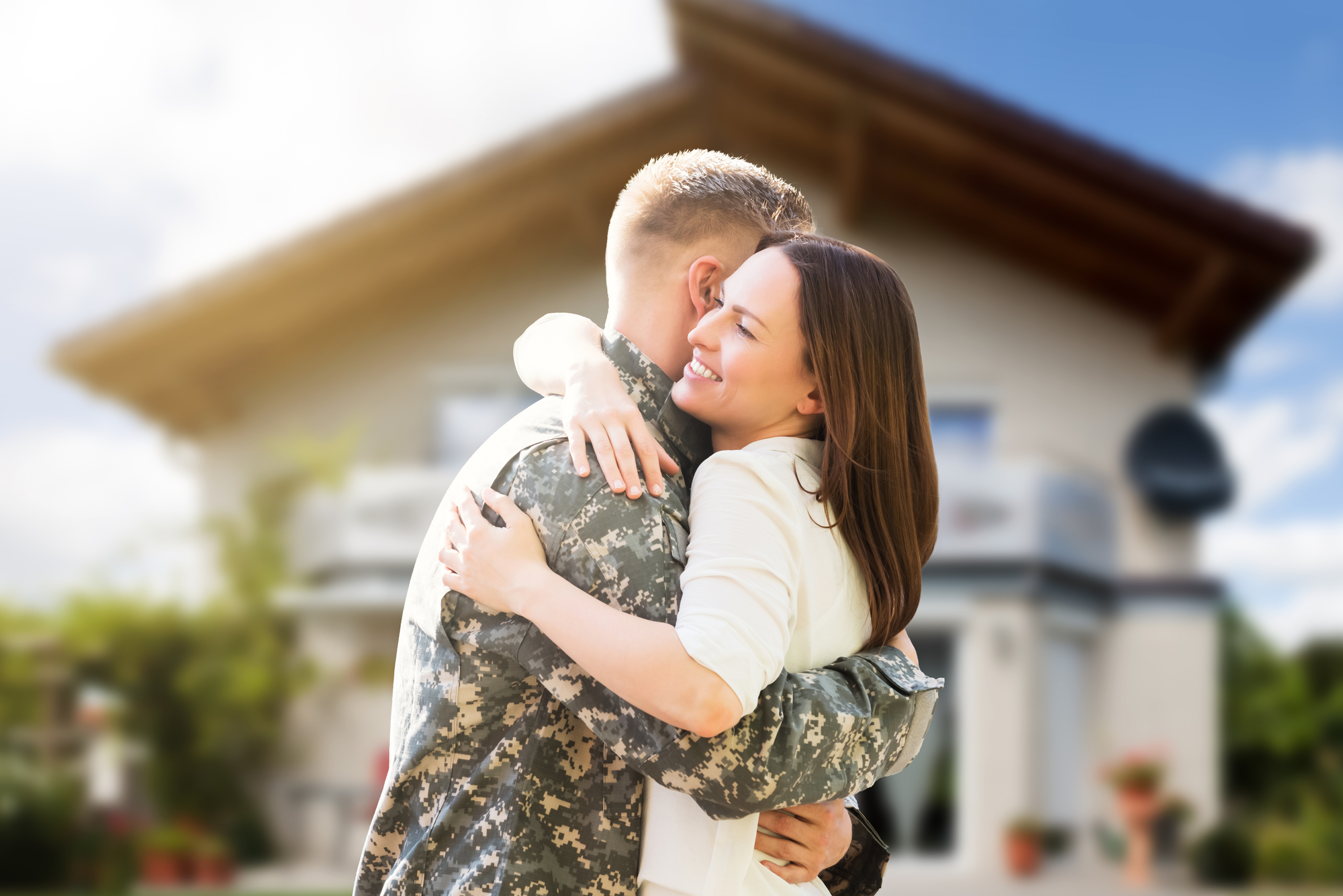 An army soldier hugs their significant other in front of a house.