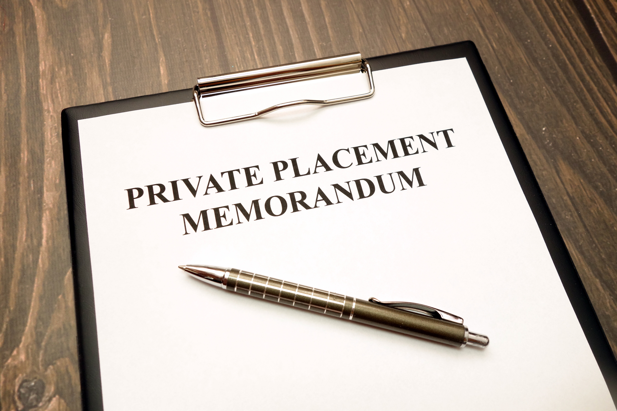 A document titled “private placement memorandum” is attached to a clipboard with a pen sitting on top of it.