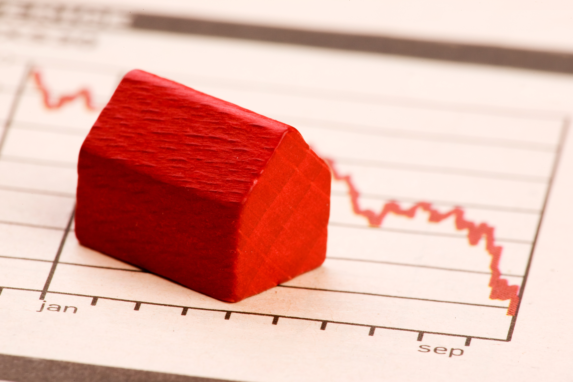 A tiny red house model sits on a graph with a red line showing a downward trend.