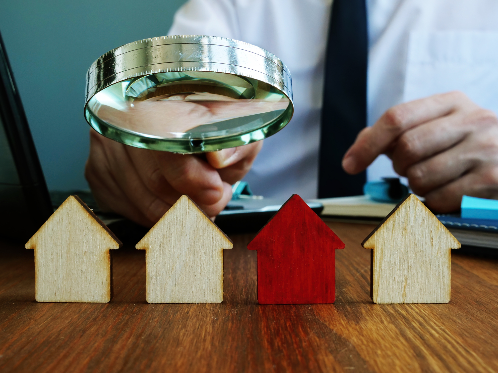 A real estate investor hovering over four model houses with a magnifying glass.