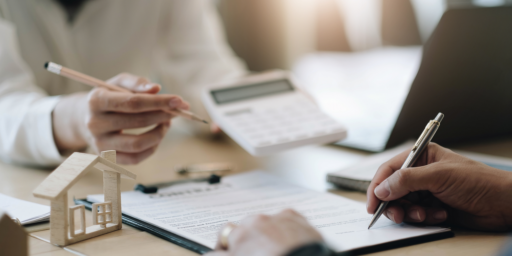 A broker and investor sit across from one another, one signing a document for their real estate acquisition fees.